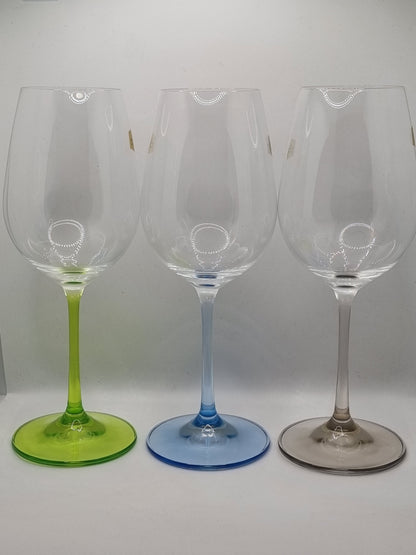 Set of three white wine glasses with blue, green and grey stems on a light grey background