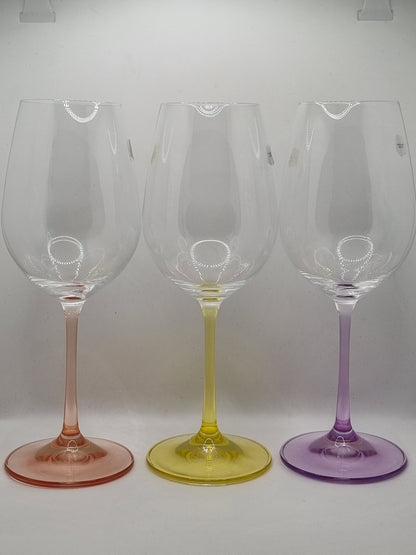 Set of three white wine glasses with red, purple and yellow stems on a light grey background