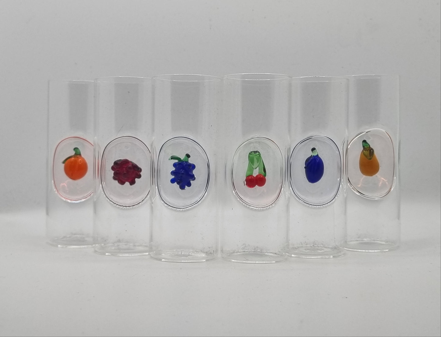 Set of clear glass shot glasses with glass fruit designs on a white background