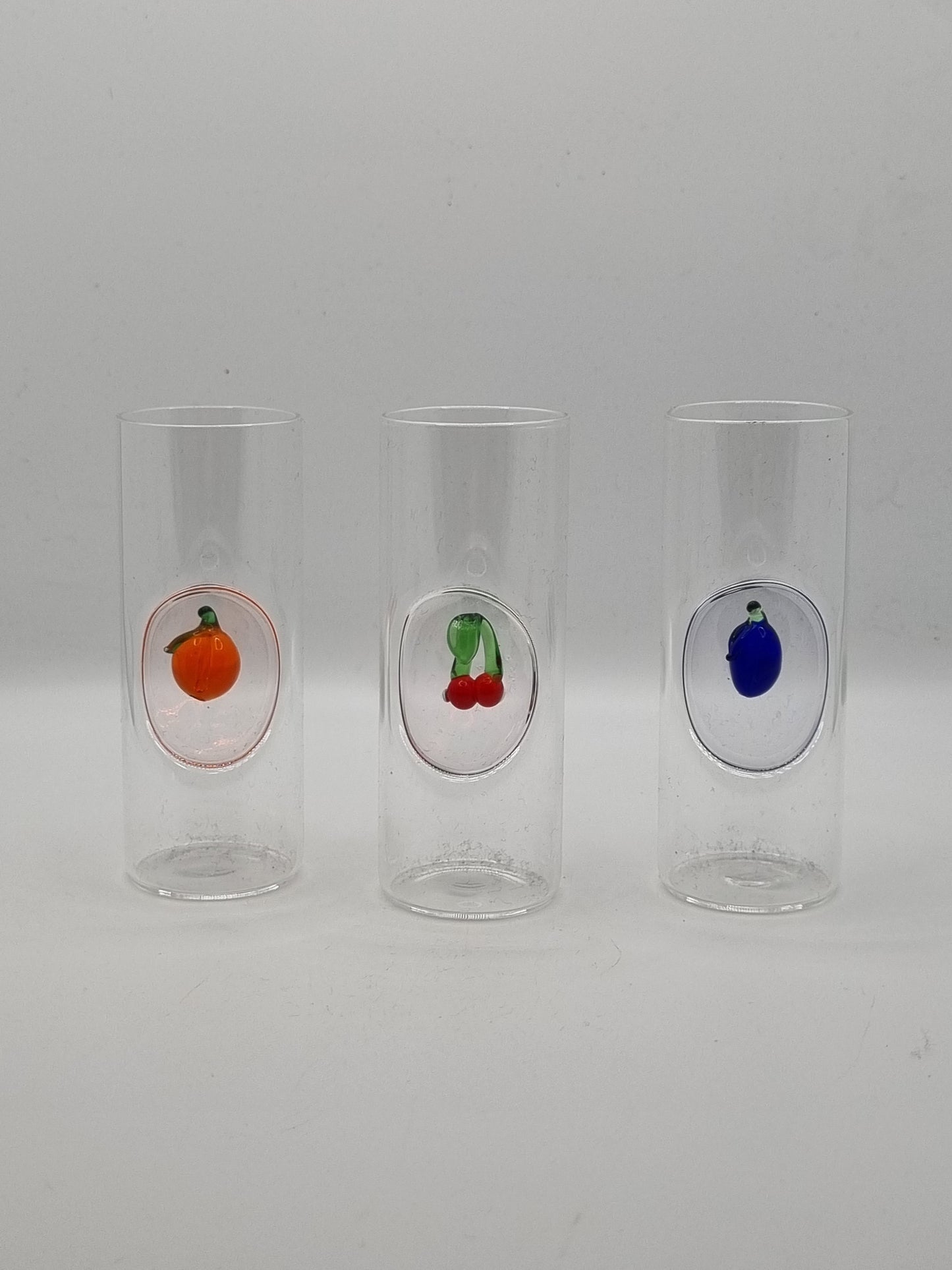 Three small round shot glass with colourful fruit insets - blue plum, red cherries and an orange