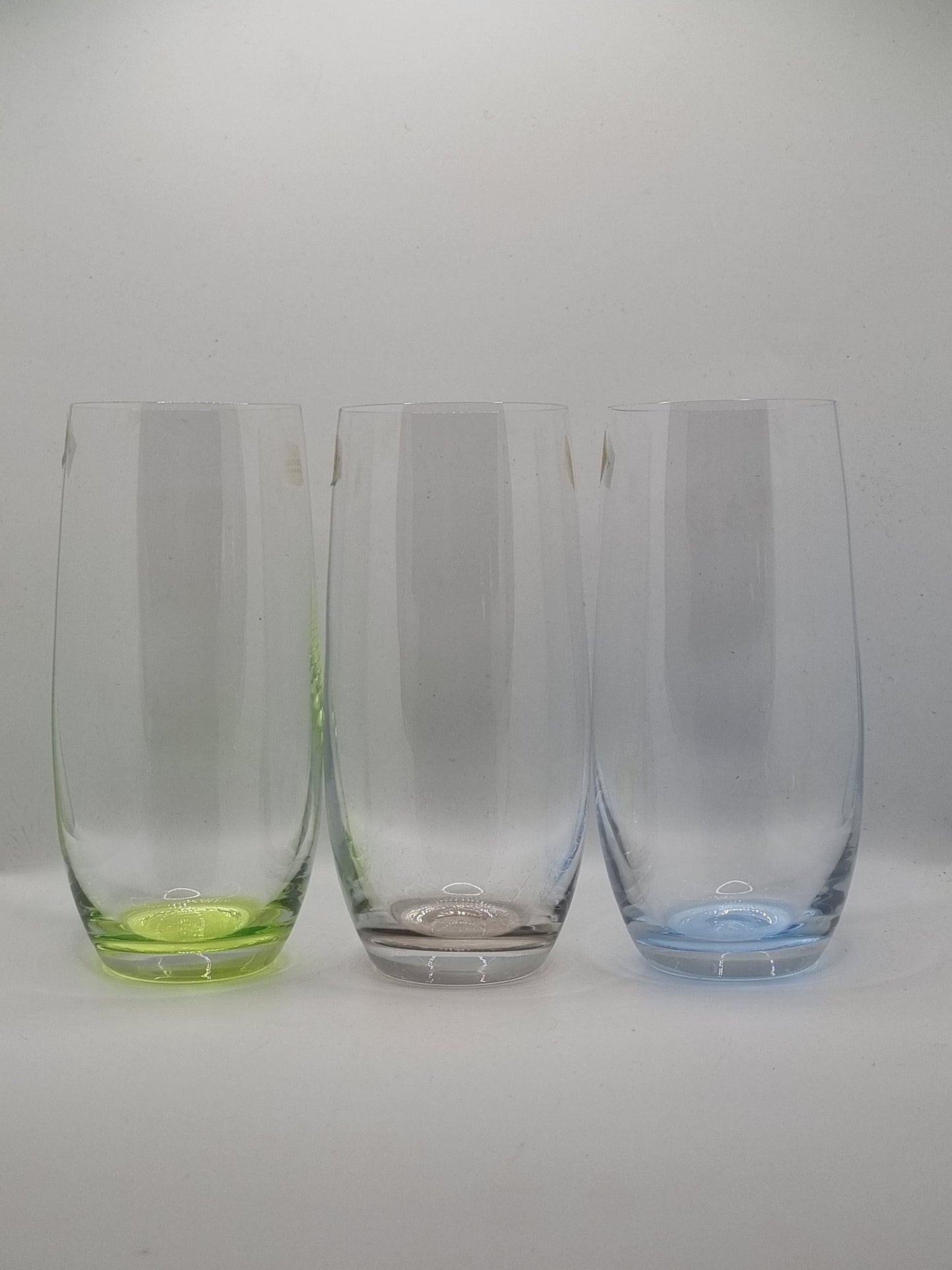 Set of three clear glass tumblers with blue, green and grey base on a white background